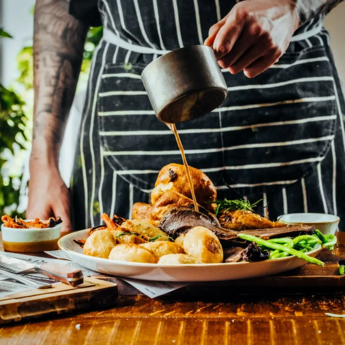 Chef pouring gravy over a Sunday roast with Yorkshire pudding and roast potatoes at The Hercules Pillars