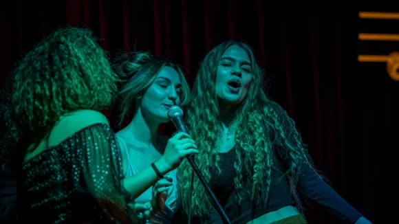 Three women singing karaoke on stage at The Flying Horse pub on Wilson Street, EC2A, near Liverpool Street