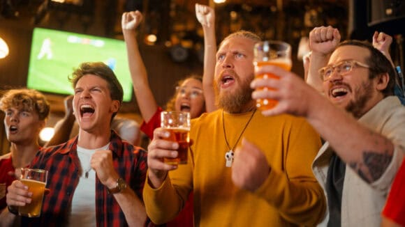 Group of football fans cheering and celebrating at a pub during Champions League match.