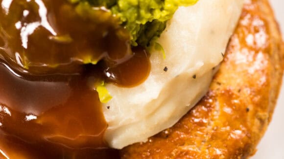 Close-up of a gourmet burger with mashed potato, guacamole, and gravy.