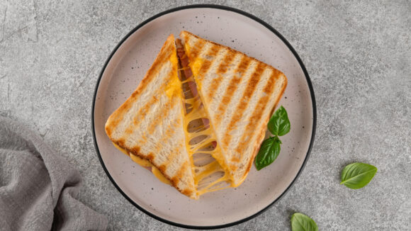 Grilled cheese sandwich with melted cheese on toasted bread, garnished with basil leaves.