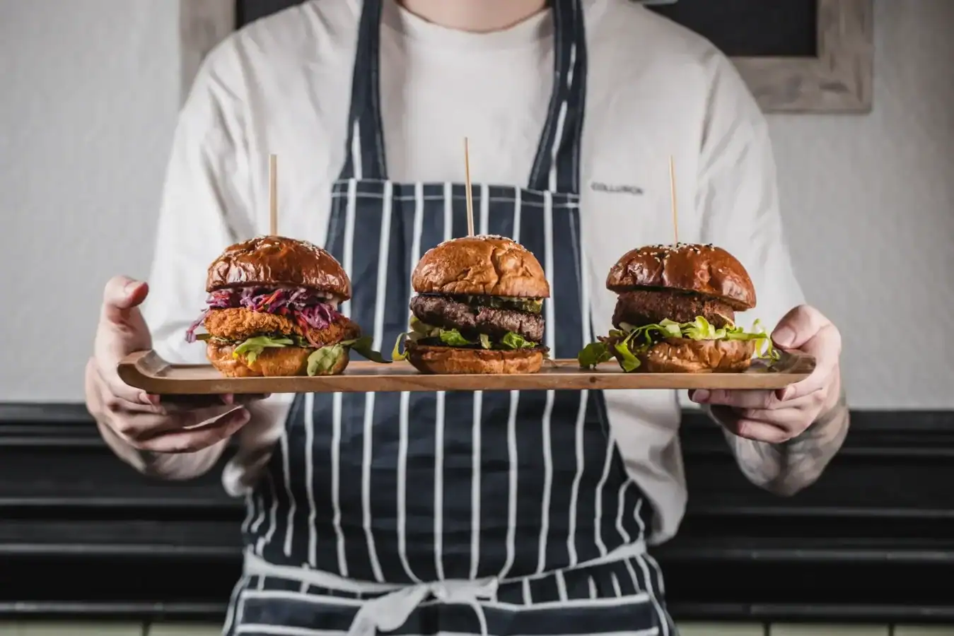 Chef holding a tray of three gourmet burgers with fresh ingredients.