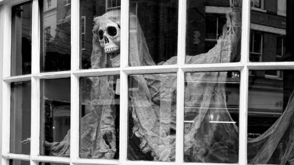 Decorative skeleton figure behind a window with draped fabric for Halloween.