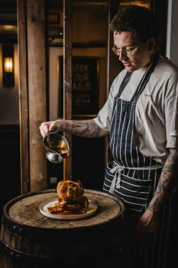 Bartender pouring sauce over a roasted chicken at The Flying Horse pub.