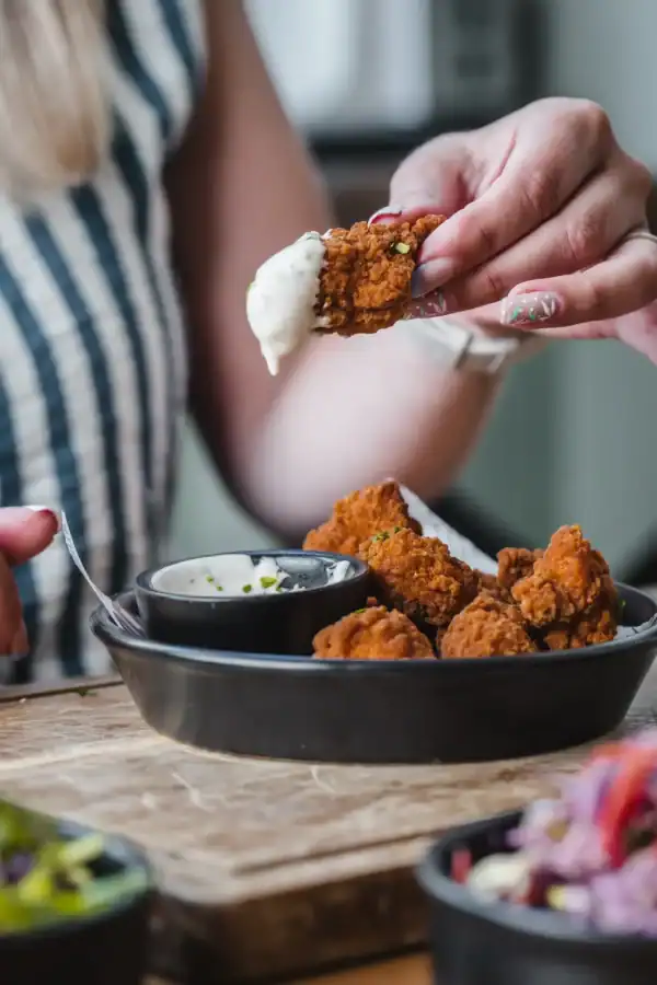 Person holding a crispy chicken bite with dipping sauce at The Flying Horse pub.